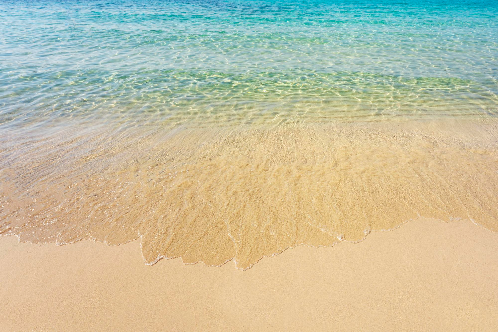The image shows a beach with golden sand and crystal clear sea.